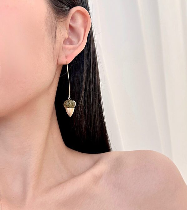 A woman wearing a pair of E102636 (Green/Gold) earrings with a heart shape.