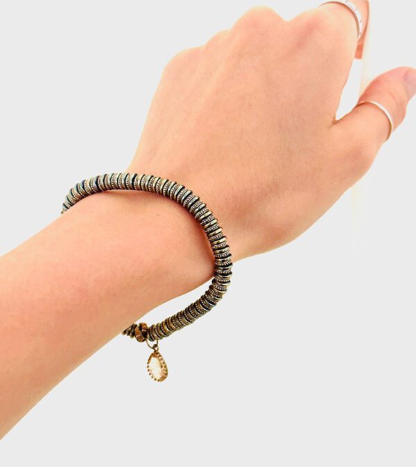 A woman's hand holding a B1014 bracelet with a gold charm.