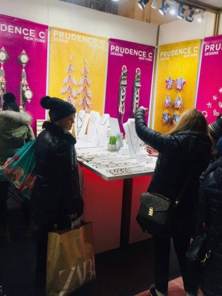 A group of people standing in front of a display by a Jewelry Designer.